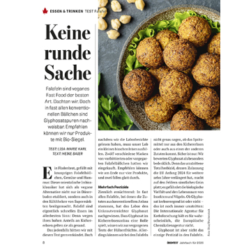 Falafelbällchen auf grünem Salat in einer grauen Schale, darüber verstreute Kichererbsen auf dunklem Untergrund.