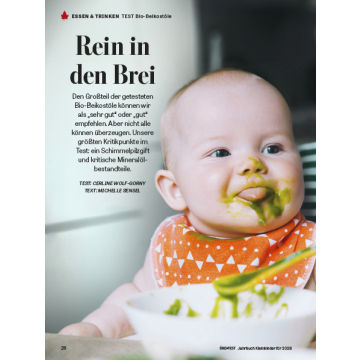 Kleinkind mit orangefarbenem Lätzchen mit weißen Dreiecken vor einem weißen Teller mit grünem Brei und Löffel, daneben Text zu Bio-Beikostölen.