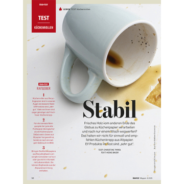 Verschmutzte weiße Tasse liegt auf einem Tisch mit Kaffeeflecken, daneben Text über Küchenrollen aus Recyclingpapier und deren Stabilität im Öko-Test Magazin.