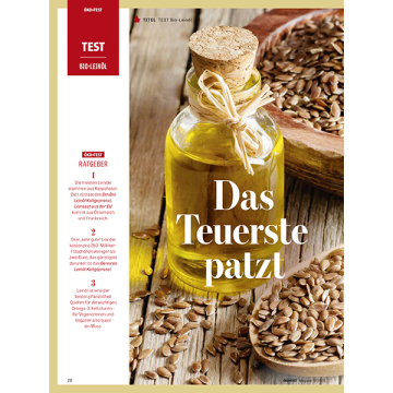 Glasflasche mit Korken und Schleife gefüllt mit gelbem Bio-Leinöl, umgeben von Leinensamen auf Holzuntergrund, Text 'Das Teuerste patzt'