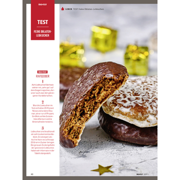 Nahaufnahme von zwei Lebkuchen, einer mit Schokoladenüberzug und Biss, der andere mit Zuckerguss, im Hintergrund goldene Geschenkboxen und ein goldener Stern auf grauem Untergrund.